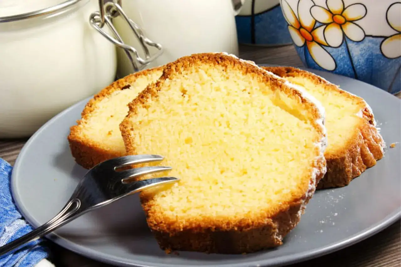 Tranches de moelleux gâteau au yaourt sur une assiette grise, avec une fourchette et un pot en verre en arrière-plan.