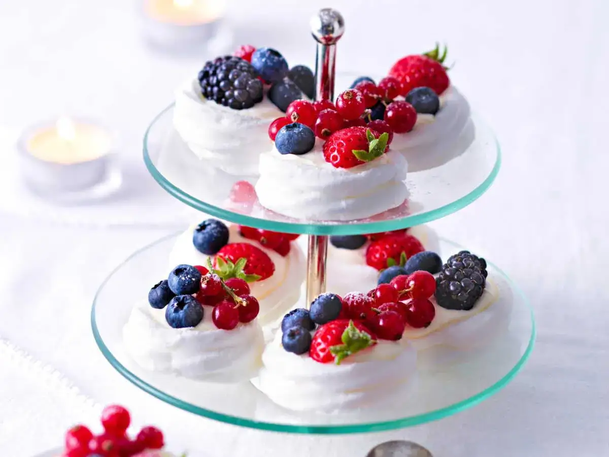 Délicieux mini pavlovas garnis de fruits rouges frais, présentés sur un présentoir à deux étages.