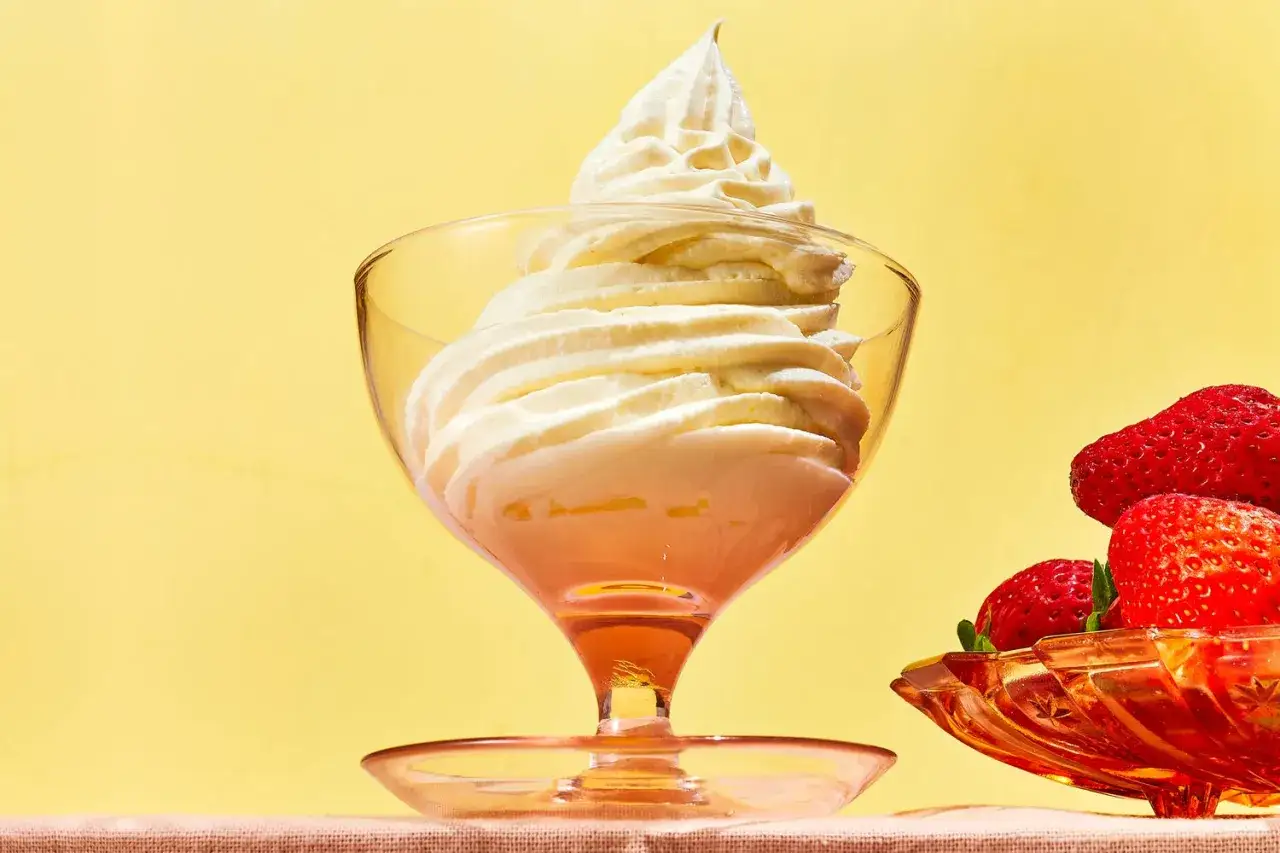Un délice de crème chantilly dans une coupe en verre, accompagné de fraises rouges éclatantes.