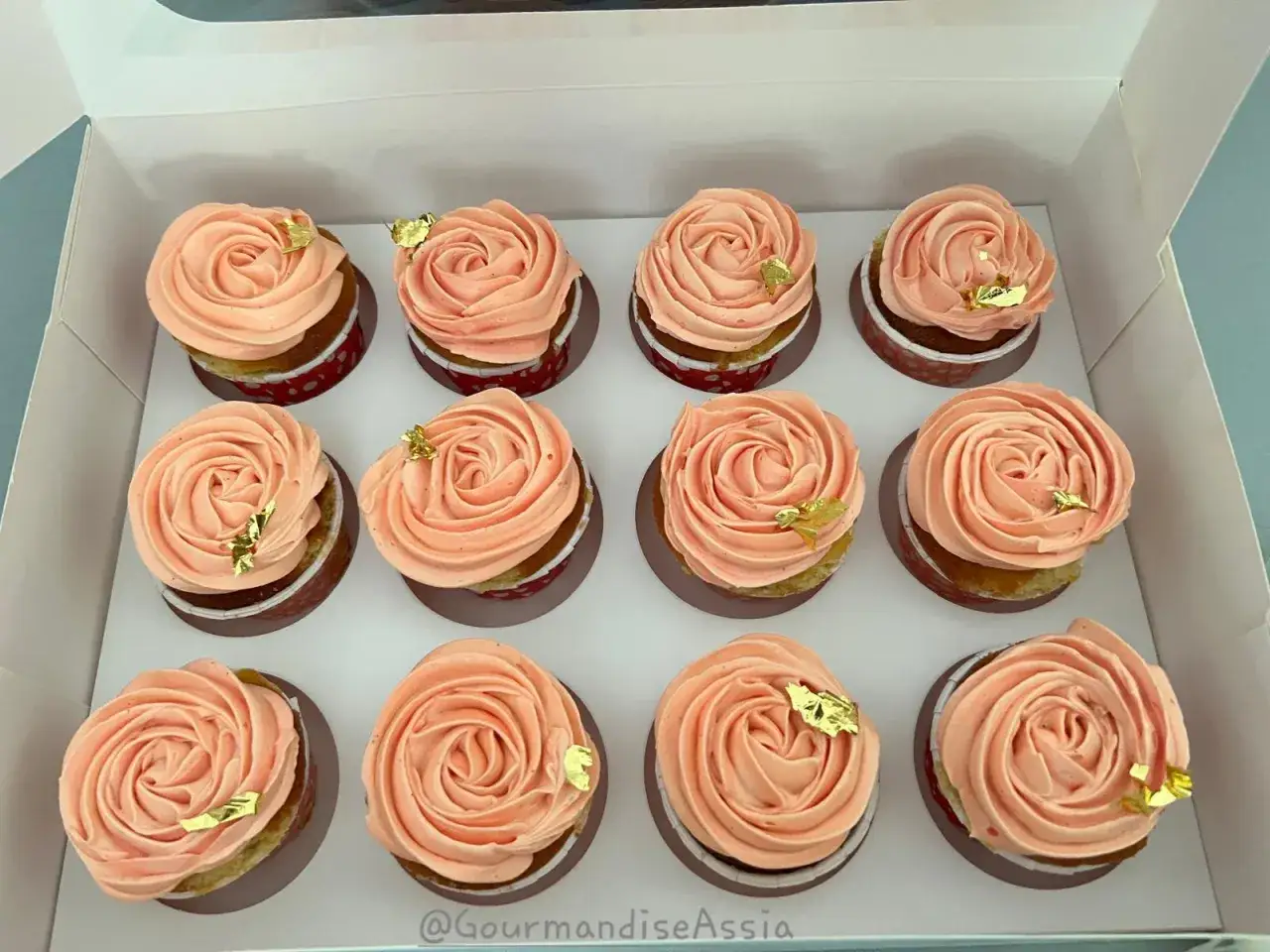 Douze cupcakes d&eacute;cor&eacute;s d'une d&eacute;licate cr&egrave;me au beurre, saupoudr&eacute;s de sucre glace et de feuilles d'or comestibles.