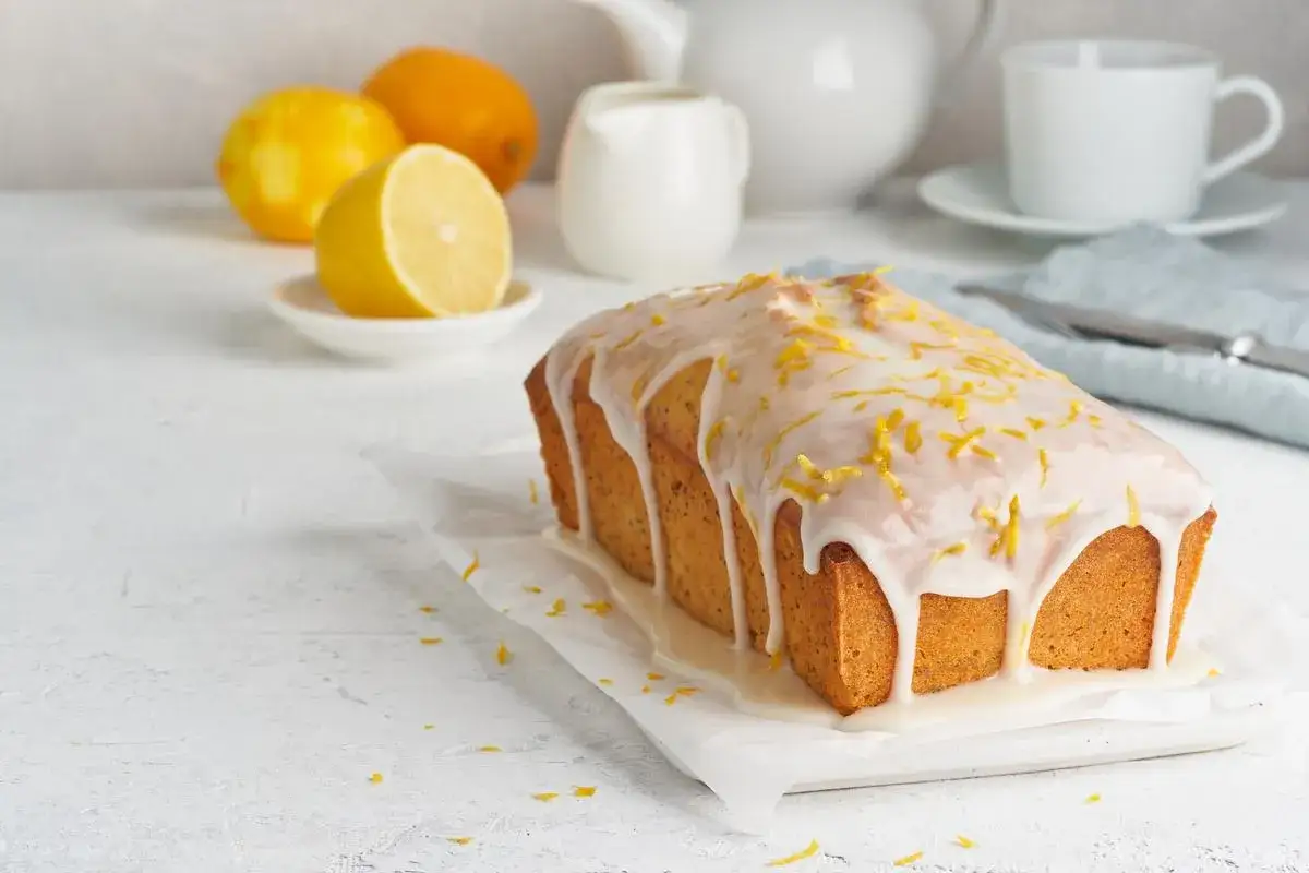 Gâteau au citron avec glaçage sucre glace facile, décoré de zestes. Des citrons et une théière en arrière-plan.