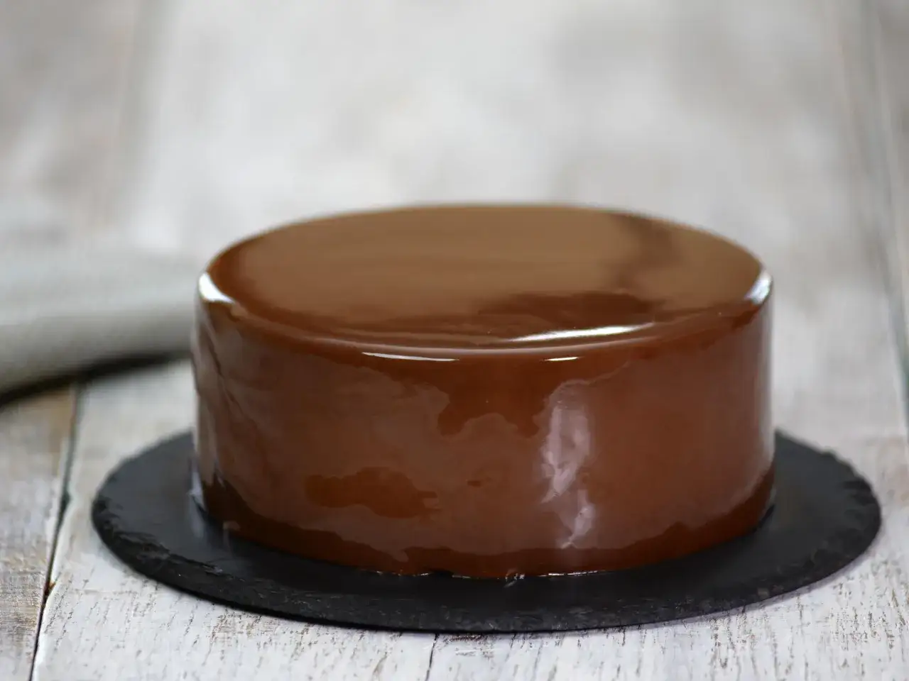 Gâteau rond avec un glaçage éclair chocolat brillant, posé sur une assiette noire.