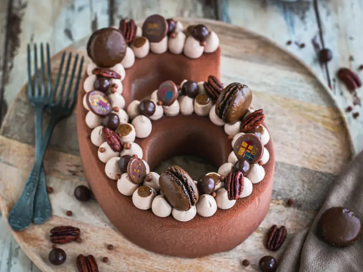 Gâteau en forme de 6, décoré de ganache, macarons, noix de pécan et chocolats. Parfait pour un anniversaire gourmand.