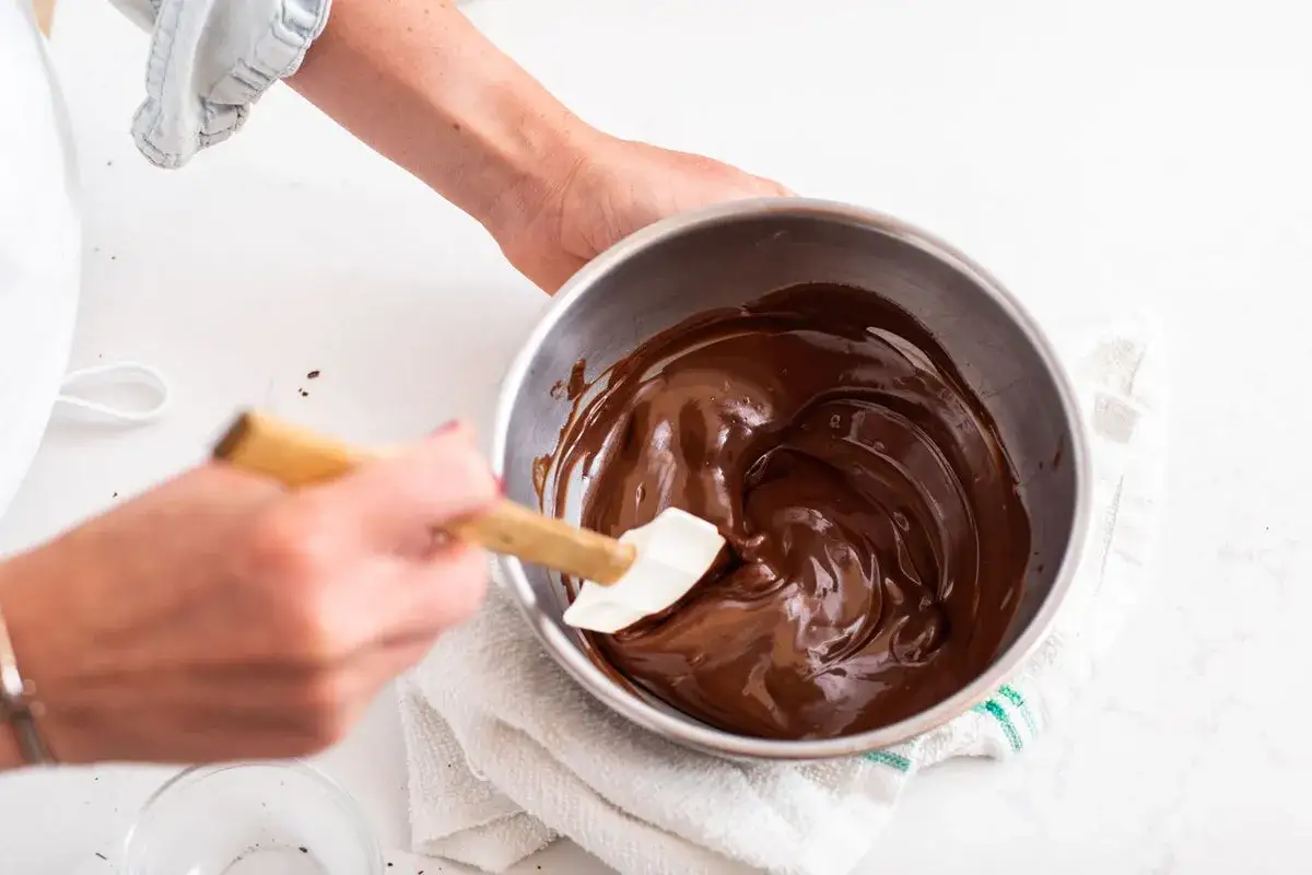 Mains remuant du chocolat fondu dans un bol en m&eacute;tal avec une spatule. Une &eacute;tape cl&eacute; pour savoir comment faire fondre du chocolat.