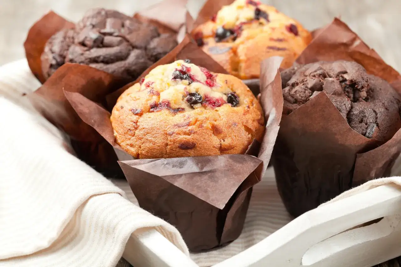 Muffins aux fruits rouges et au chocolat, certains gonflés de travers, dans un panier en bois.