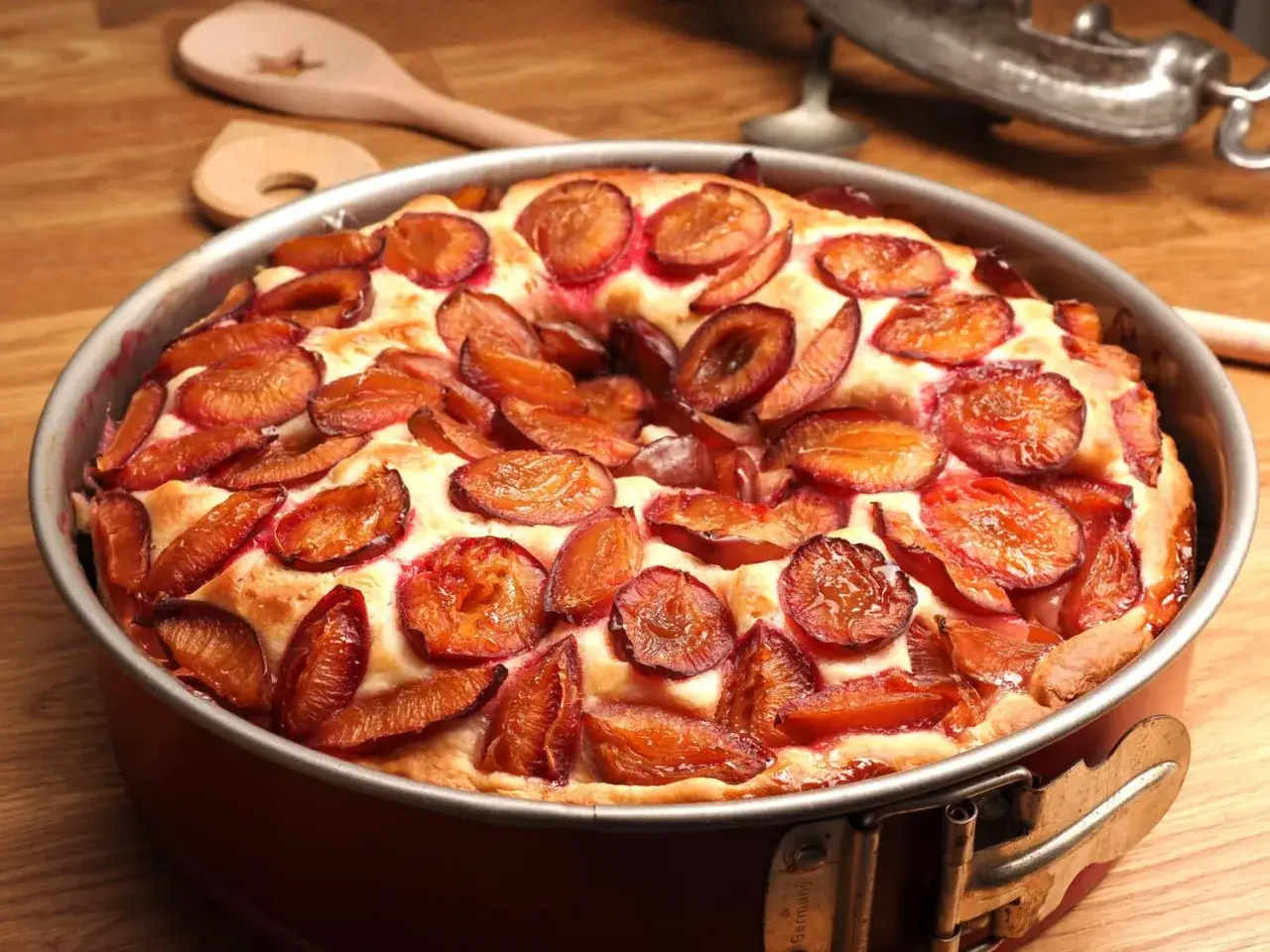 Un délicieux clafoutis aux prunes, tout juste sorti du four, dans son moule à charnière. Les prunes caramélisées brillent sur la pâte dorée.