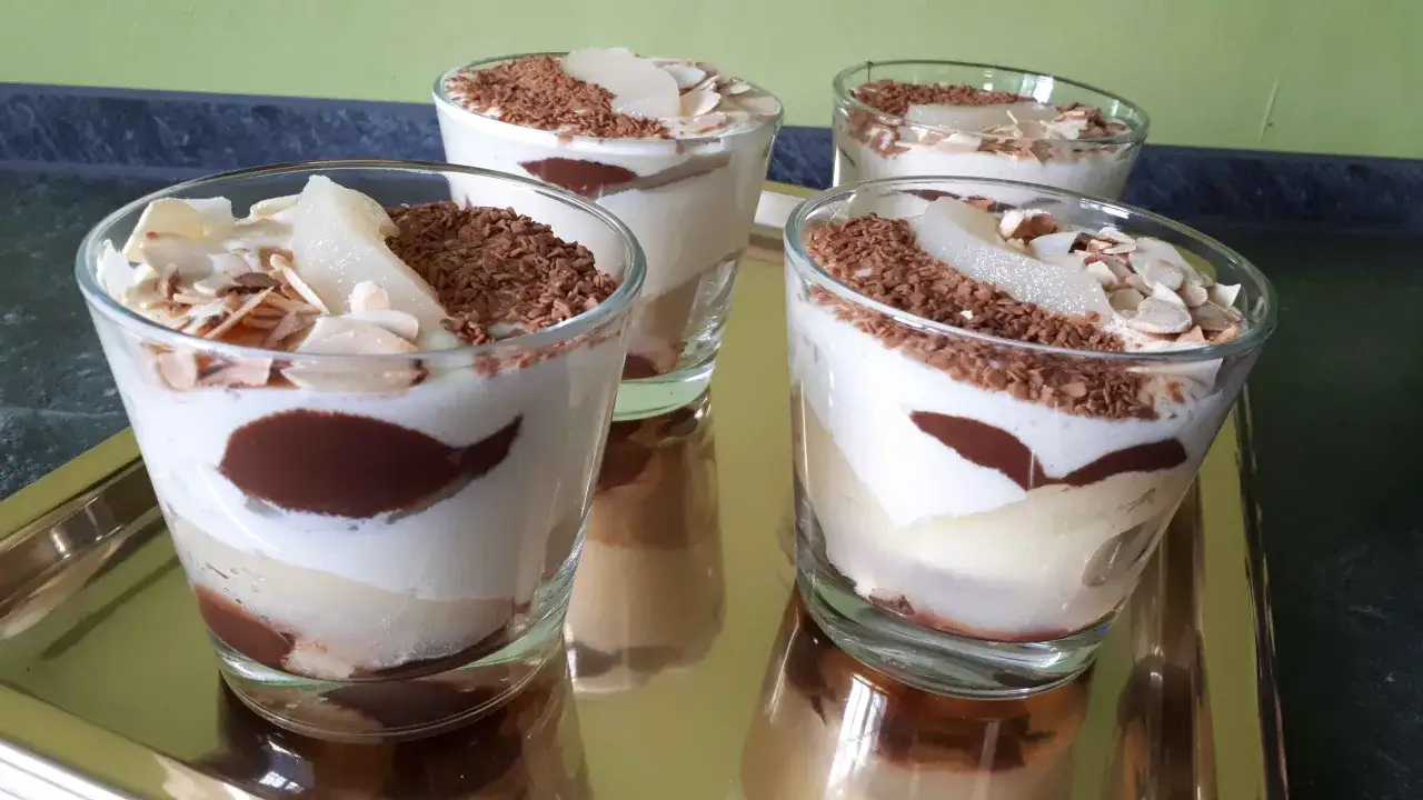 Quatre verrines poire chocolat mascarpone, garnies de copeaux de chocolat et d'amandes effilées. Un délice gourmand !