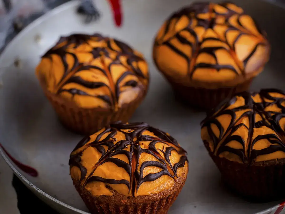 Quatre cupcakes d'Halloween orange vif, décorés d'une toile d'araignée en chocolat noir. Parfait pour une fête effrayante !