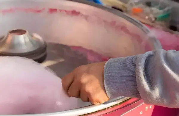 Main d'une personne récoltant du sucre filé rose, étape clé pour savoir comment faire du sucre à barbe à papa.