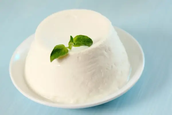Un dôme de ricotta crémeuse, garni d'une feuille verte, sur une assiette blanche. Découvrez les ricotta bienfaits pour une alimentation saine.
