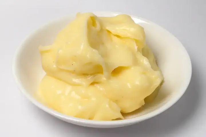 Crème pâtissière onctueuse et dorée, prête à garnir éclairs et millefeuilles. Petits points noirs de vanille visibles.