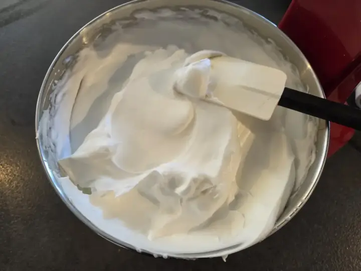 Une spatule mélange une épaisse crème chantilly dans un bol en acier inoxydable.