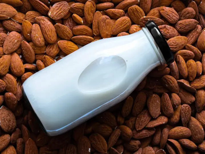 Bouteille de lait d'amande maison posée sur un lit d'amandes entières.